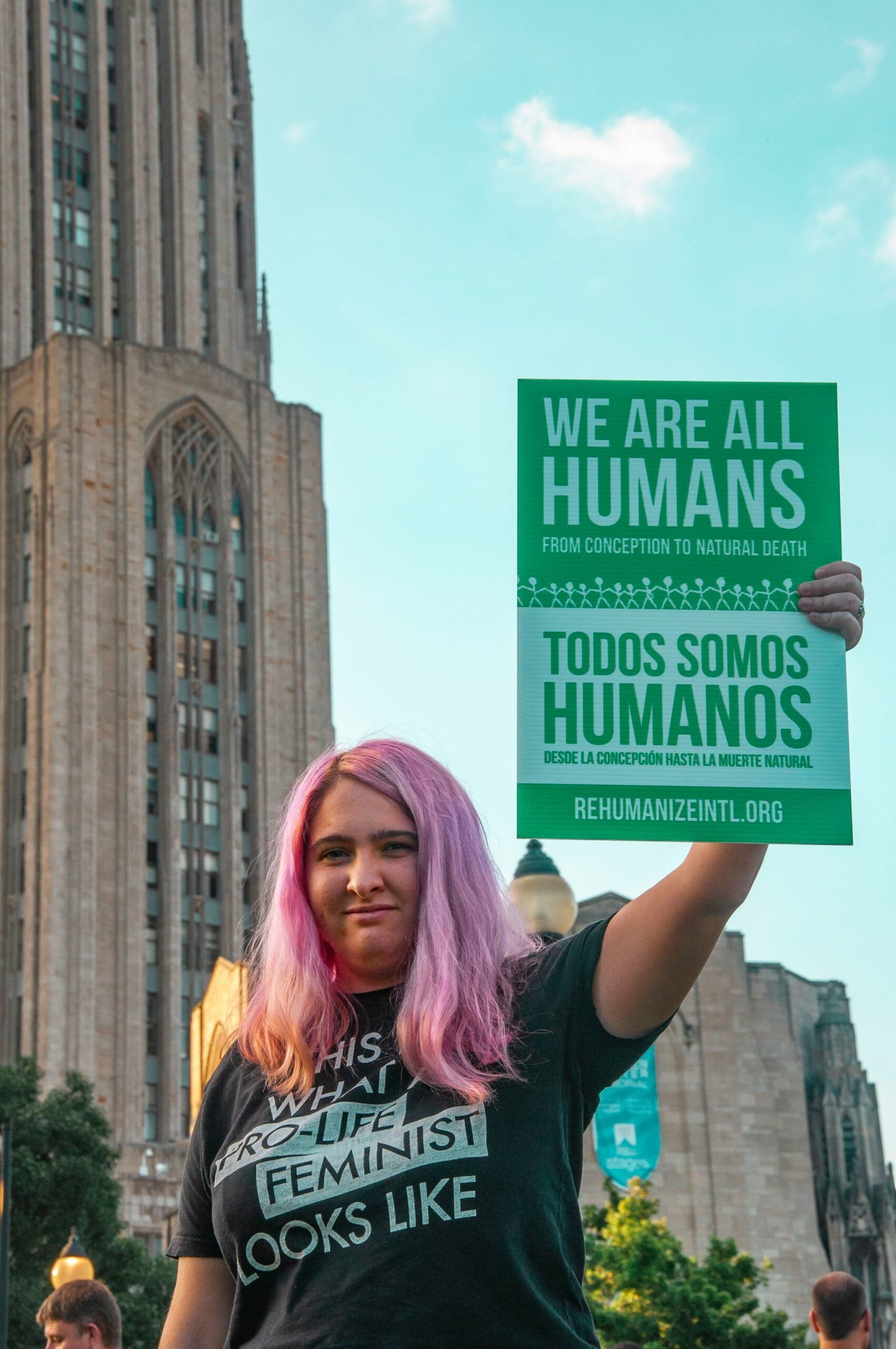 woman with pink hair holding green placard